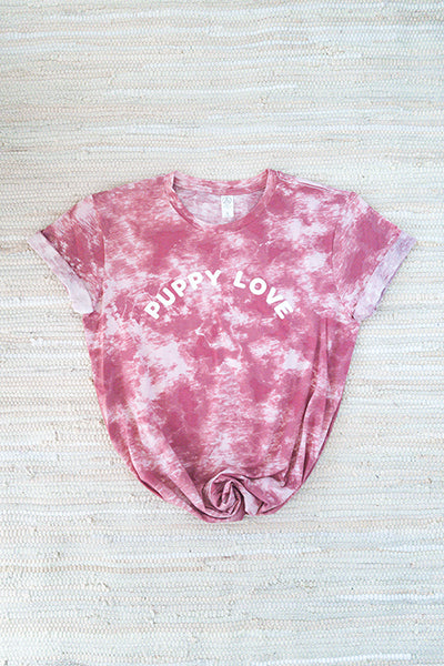 flat image of pink tie-dye 100% cotton alternative tee screen-printed with white puppy love in an arched font