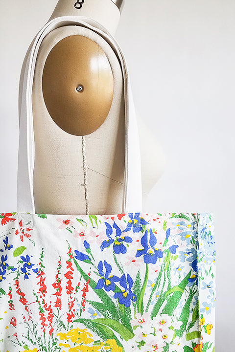 Zoomed in image of a vintage textile market hanging on the shoulder of a dress form in front of a white background. The tote is sustainably made from 100% cotton fabrics. The main fabric is a colorful floral vintage curtain and the shoulder straps are an organic cotton canvas