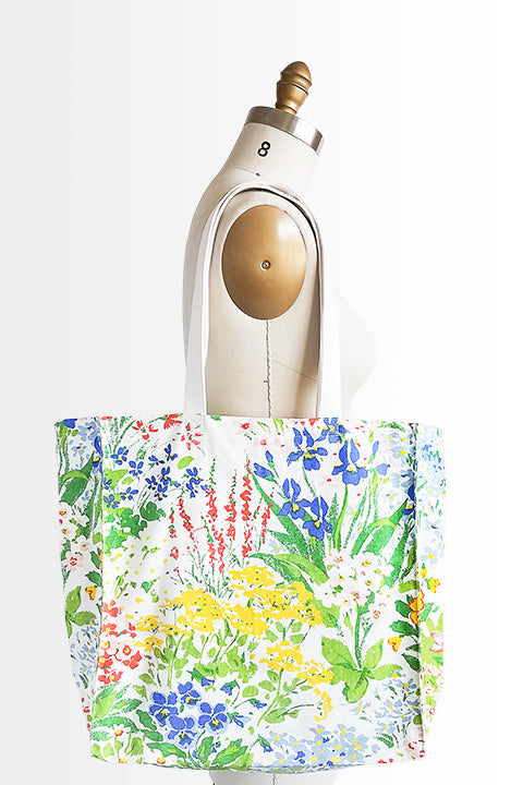 Image of a vintage textile market hanging on the shoulder of a dress form in front of a white background. The tote is sustainably made from 100% cotton fabrics. The main fabric is a colorful floral vintage curtain and the shoulder straps are an organic cotton canvas